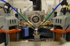 View of the experiment at the PETRA III beamline P01 (in X-ray beam direction): The sample on the round table in the centre of the picture is connected to microwave measuring tips. The X-rays emitted by the sample are analysed at the end with a detector. Electromagnets with iron yokes around the sample table generate a magnetic field at the sample location to align the magnetisation in the sample